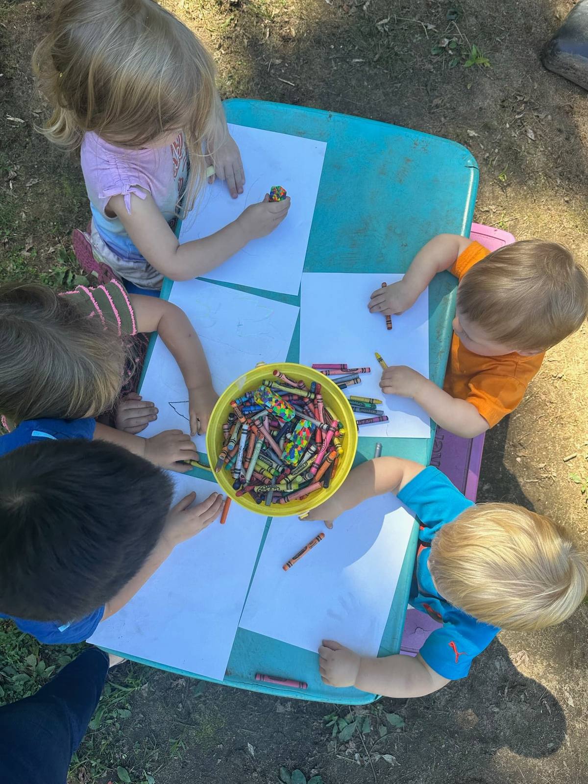 Children drawing with crayons at an outdoor table