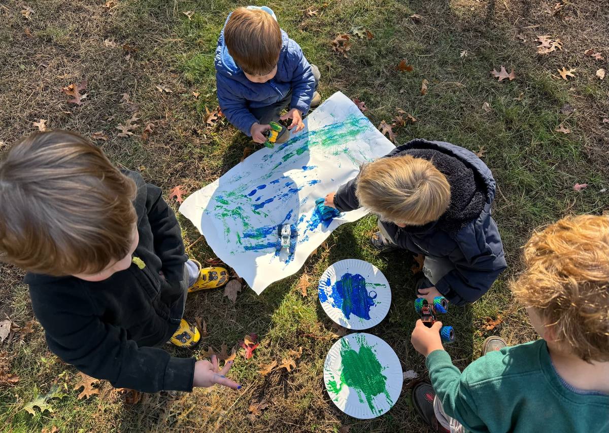 Children painting outdoors with toy trucks